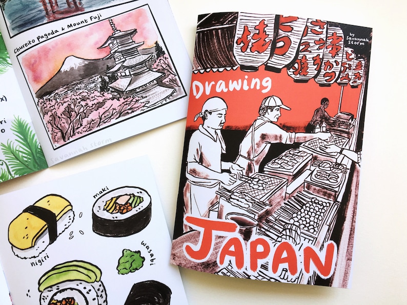 A printed zine called 'Drawing Japan' with a black and red cover showing a Japanese yakitori food stall. Also interior pages show mount Fuji and a pagoda, and some sushi.