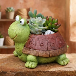 May include: A turtle-shaped planter with a textured light green head and limbs, featuring a dark reddish-brown shell that serves as a container. The shell holds a cluster of green and reddish-tipped succulent plants nestled among small white stones.