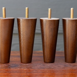 May include: Four tapered wooden furniture legs with brass threaded inserts. The legs are a rich brown color and have a smooth finish. They are designed for easy attachment to furniture.