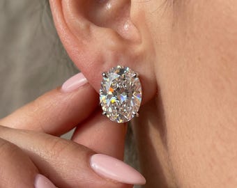 May include: A single oval-cut clear gemstone stud earring set in a silver-toned metal prong setting. The faceted stone features a brilliant cut that reflects light, creating a sparkling appearance against the earlobe, secured with a metal post.
