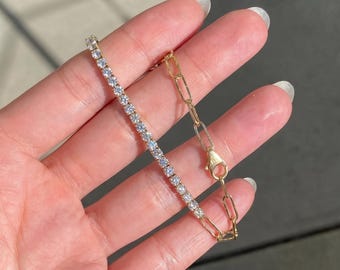 May include: A gold-toned bracelet featuring a dual-style design, with one half composed of a continuous row of small, clear, round-cut stones and the other half consisting of elongated, oval-shaped gold-toned metal links with a lobster clasp.