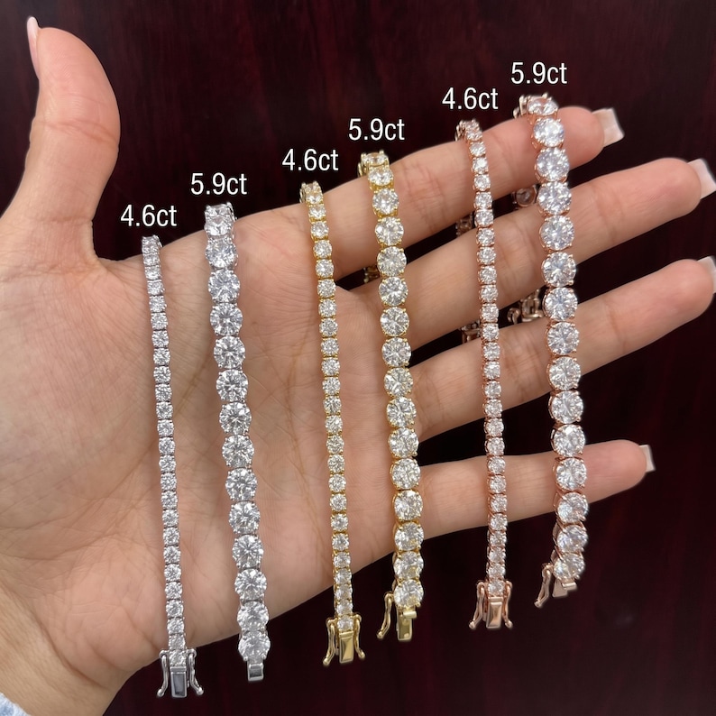 May include: Six tennis bracelets in silver, gold, and rose gold tones, each featuring round clear stones. The bracelets are labeled with weights of 4.6ct and 5.9ct. Each piece includes a metal clasp closure at the end of the stone-set chain.