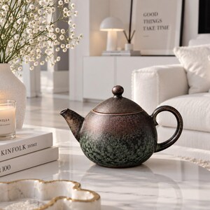 May include: A round ceramic teapot with a textured finish featuring a gradient of dark brown at the top and lid, transitioning into a mottled deep green at the base. The teapot has a curved handle, a short spout, and a matching domed lid with a knob.