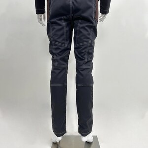 May include: A pair of dark navy blue trousers featuring prominent white contrast stitching along the seams, pockets, and knees. The trousers have a structured fit with reinforced paneling on the upper thighs and a straight leg design.