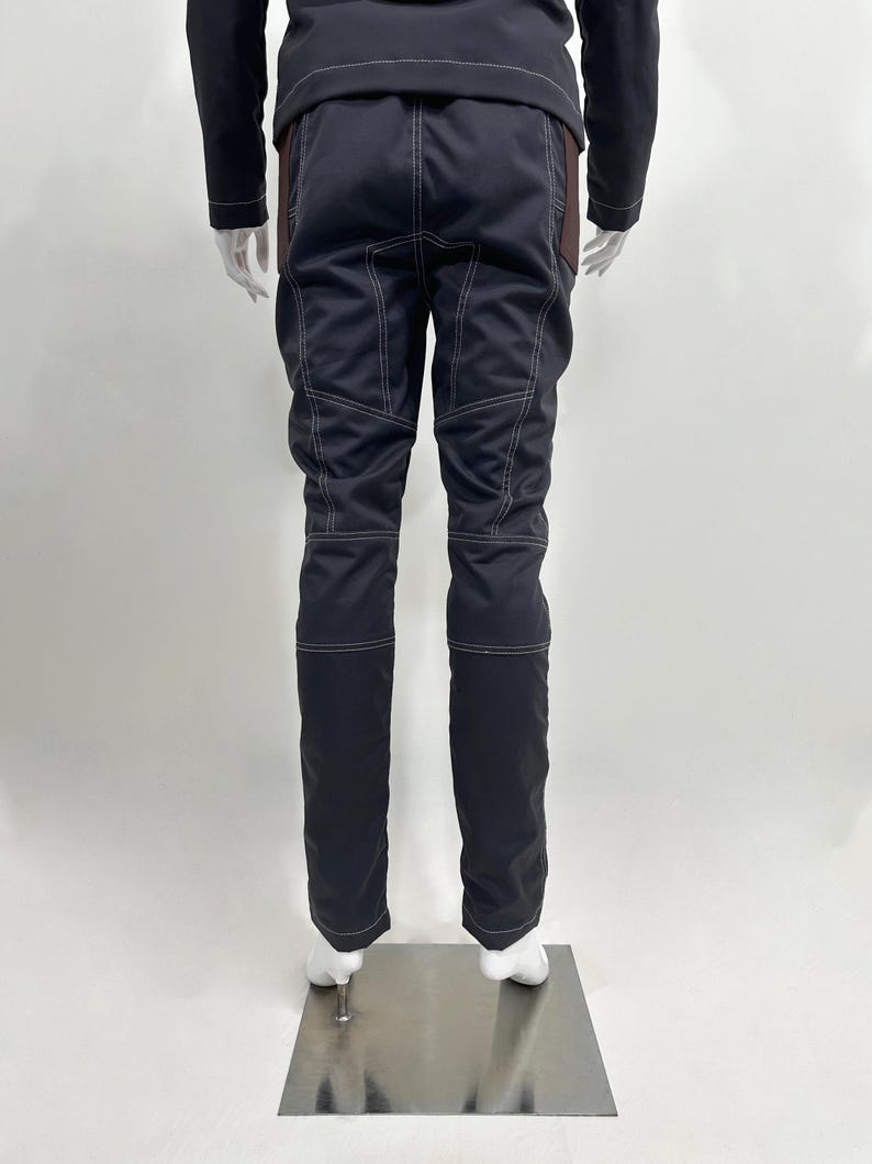 May include: A pair of dark navy blue trousers featuring prominent white contrast stitching along the seams, pockets, and knees. The trousers have a structured fit with reinforced paneling on the upper thighs and a straight leg design.