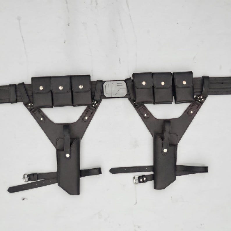 May include: A black utility belt featuring two symmetrical holster attachments, each equipped with three small rectangular pouches with snap closures and a vertical holster sleeve. The central buckle is a rectangular silver-toned metal piece.