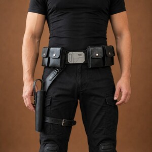 May include: A black utility belt featuring multiple rectangular pouches with silver-toned snap closures, a central metallic buckle with geometric detailing, and an attached drop-leg holster with a buckled thigh strap, worn over black trousers.