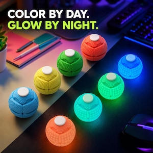 Può includere: Sette fidget toy sferici con superfici testurizzate e pulsanti circolari bianchi sulla parte superiore. Tre non sono illuminati in blu, giallo e verde, mentre quattro brillano in arancione, turchese, verde e blu. Testo: COLOR BY DAY. GLOW BY NIGHT.