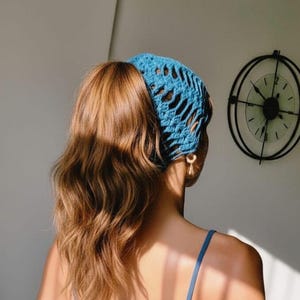 Pode incluir: Um acessório de cabelo em crochê azul brilhante com um padrão aberto usado na cabeça. O acessório apresenta um design texturizado e com nós que cobre o topo da cabeça, proporcionando uma fixação segura para o cabelo com leveza.