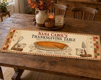 May include: A rectangular table runner featuring a cream-colored background with a patchwork border. The text reads NANA CAROL'S THANKSGIVING TABLE, MADE WITH LOVE, SERVED SINCE 1993, and CAROL'S SPICED PUMPKIN PIE, with illustrations of a pie, whisk, and measuring cup.