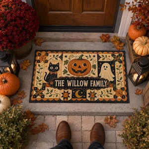 May include: A rectangular Halloween-themed doormat featuring a black cat, a jack-o'-lantern, and a ghost. The text THE WILLOW FAMILY is printed in the center. The border has a quilt-like pattern with stars, leaves, and a crescent moon.