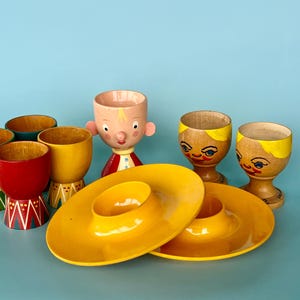 An array of 9 fun egg cups - wood egg cups from Germany, Norway, Italian boy - Sevi and two Mepal Rosti egg cups from Denmark. Useful & fun.