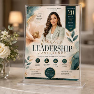 May include: A clear acrylic sign holder displaying a Women's Leadership Conference flyer. The flyer features a portrait of a person, a large peach flower, teal watercolor accents, and gold text. It includes event details, date, and contact information.