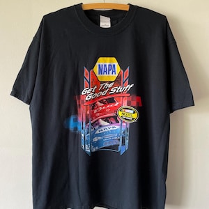 Könnte beinhalten: Ein schwarzes Kurzarm-T-Shirt mit einem Grafikdruck, der das NAPA-Logo, den Text "Get The Good Stuff" und Bilder von zwei Rennwagen zeigt. Das Design enthält ein NASCAR Nextel Cup Series-Emblem, rote Karomuster-Akzente und blaue Details.
