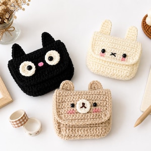 May include: Three small crochet bags shaped like animals. One is black with cat ears and white circular eyes, one is cream with rabbit ears, and one is light brown with bear ears. Each bag features embroidered facial details and pink cheeks.