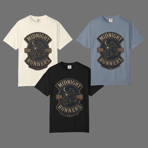 Può includere: Tre magliette a maniche corte in crema, blu e nero. Ogni maglietta presenta una grafica centrale di un motociclista sotto una luna crescente con il testo "MIDNIGHT RUNNERS", "EST. 2015" e "RIDE FAST LIVE FREE" in un emblema circolare.