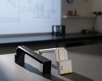 Może przedstawiać: Czarne i białe urządzenie o kanciastym kształcie przypominającym uchwyt. Biały model posiada mały czarny czujnik oraz żółty napis "FibrePulse" na przedniej ściance. Oba przedmioty mają geometryczną konstrukcję w kształcie mostka.