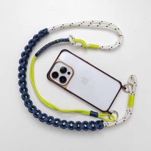 May include: A smartphone with a clear case attached to a decorative lanyard. The lanyard features a white rope with black speckles, a dark blue braided section, and bright neon yellow cord accents with silver-toned metal hardware rings.