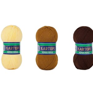 May include: Three balls of KARTOPU Super Perle yarn in shades of yellow, brown, and dark brown. Each ball is wrapped with a label featuring the brand name and product details. The yarn is likely used for knitting or crochet projects.