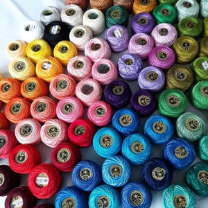 Puede incluir: Una colección de carretes de hilo de bordar de colores, dispuestos en un patrón circular. Los carretes son de varios tonos de rojo, naranja, amarillo, verde, azul, morado y marrón.