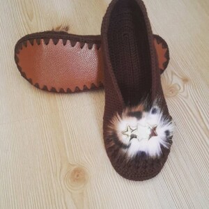 May include: A pair of brown crocheted slippers with a leopard print fur pom-pom and gold star embellishments.