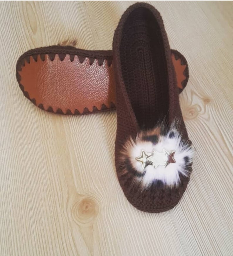 May include: A pair of brown crocheted slippers with a leopard print fur pom-pom and gold star embellishments.