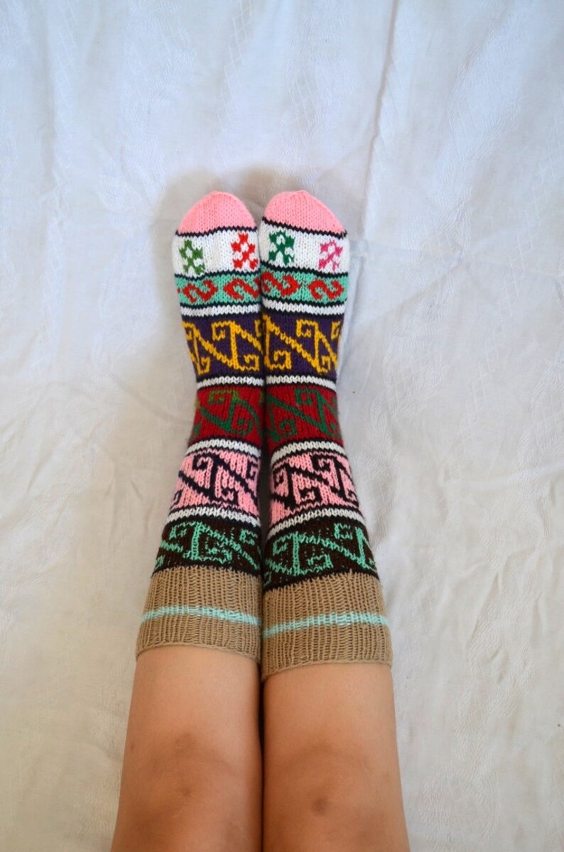 May include: A pair of colorful knitted socks with a geometric pattern in shades of pink, brown, green, white, and purple. The socks are worn on a person's legs.