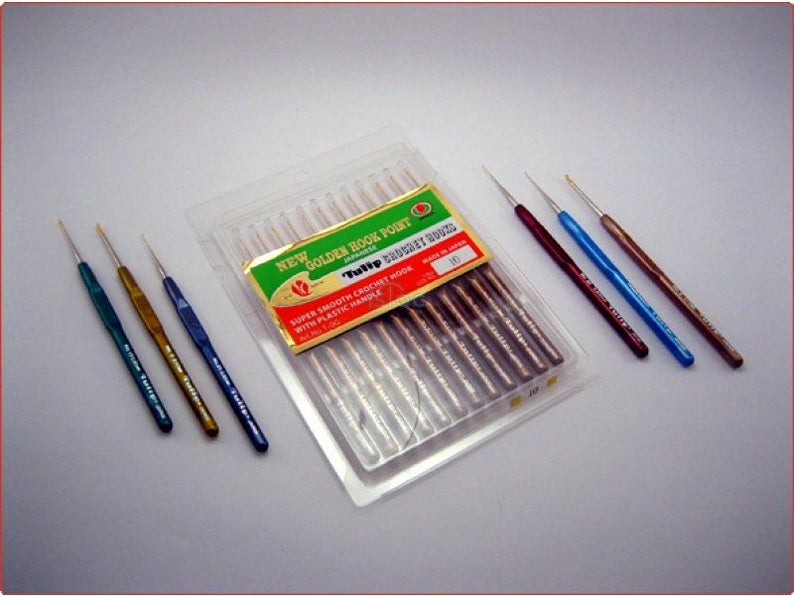 May include: A pack of 10 gold crochet hooks with plastic handles. The hooks are in a clear plastic package with a green and red label that says "New Golden Book Point Tulip Crochet Hook". There are also three individual crochet hooks in green, gold, and blue.