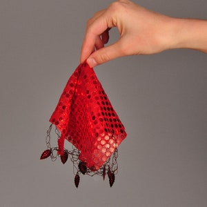 Puede incluir: Una tela roja con lentejuelas y un borde de flecos. La tela está sostenida por una mano.