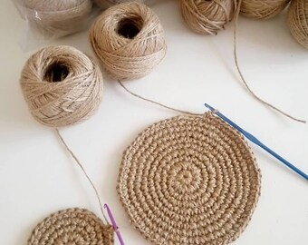 May include: Two crocheted jute coasters, one larger than the other, with a ball of jute twine and a crochet hook.