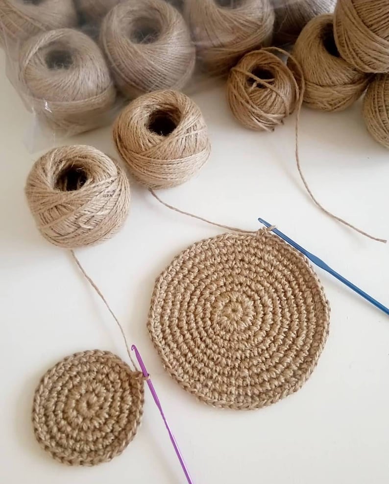 May include: Two crocheted jute coasters, one larger than the other, with a ball of jute twine and a crochet hook.