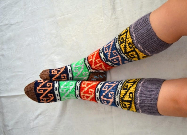 May include: A pair of colorful knee-high socks with a geometric pattern in shades of red, blue, green, yellow, and brown. The socks are knitted and have a gray cuff.