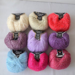 Puede incluir: Nueve ovillos de hilo con hilo de purpurina plateado. El hilo es de color crema, morado, lavanda, azul claro, rosa y rojo. Las etiquetas del hilo dicen "Simli Iplik" en texto negro.