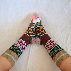 May include: A pair of colorful knitted socks with a geometric pattern in shades of brown, pink, green, red, white, and purple. The socks are folded over at the top and are worn on a person's feet.