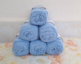 May include: A stack of six light blue cotton yarn balls on a floral patterned surface.