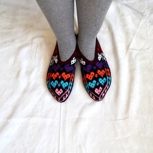 May include: A pair of colorful knitted slippers with a heart pattern. The slippers are black with orange, purple, blue, and pink hearts.