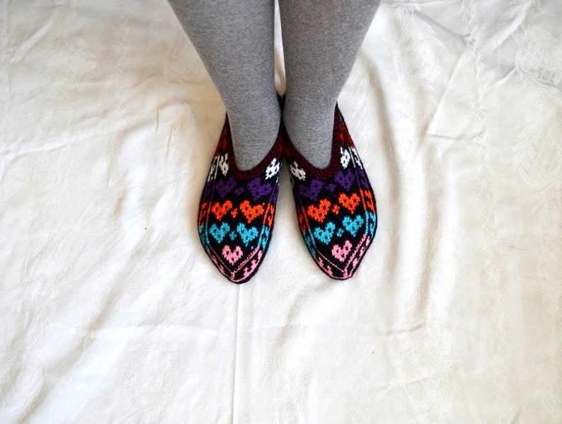 May include: A pair of colorful knitted slippers with a heart pattern. The slippers are black with orange, purple, blue, and pink hearts.