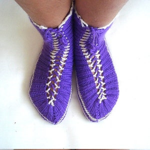 May include: Purple knitted slipper socks with white trim and a criss-cross pattern.
