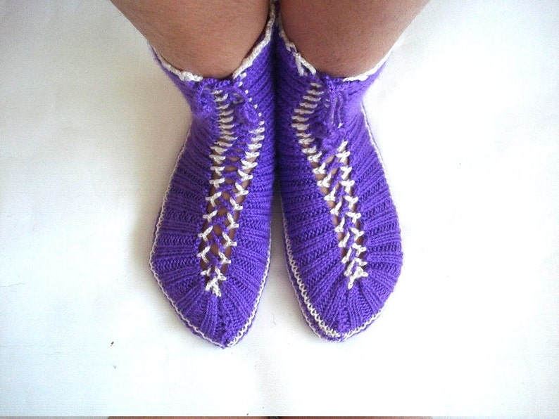 May include: Purple knitted slipper socks with white trim and a criss-cross pattern.