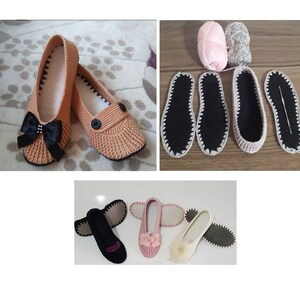 May include: A pair of crocheted slippers with black bows and buttons. The slippers are beige and have black trim. There are also two pairs of pink and black crocheted slippers with black trim.