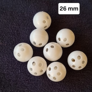 May include: Eight white plastic balls with holes, each measuring 26 mm in diameter. The balls are arranged in a semi-circle on a dark blue fabric surface.