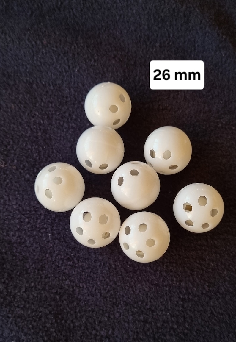 May include: Eight white plastic balls with holes, each measuring 26 mm in diameter. The balls are arranged in a semi-circle on a dark blue fabric surface.