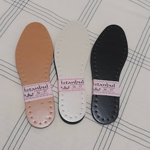 May include: Three leather shoe insoles in brown, white, and black. Each insole has a label that reads "Istanbul Ayakkabı Ke&ccedil;eleri 36-37" in pink.