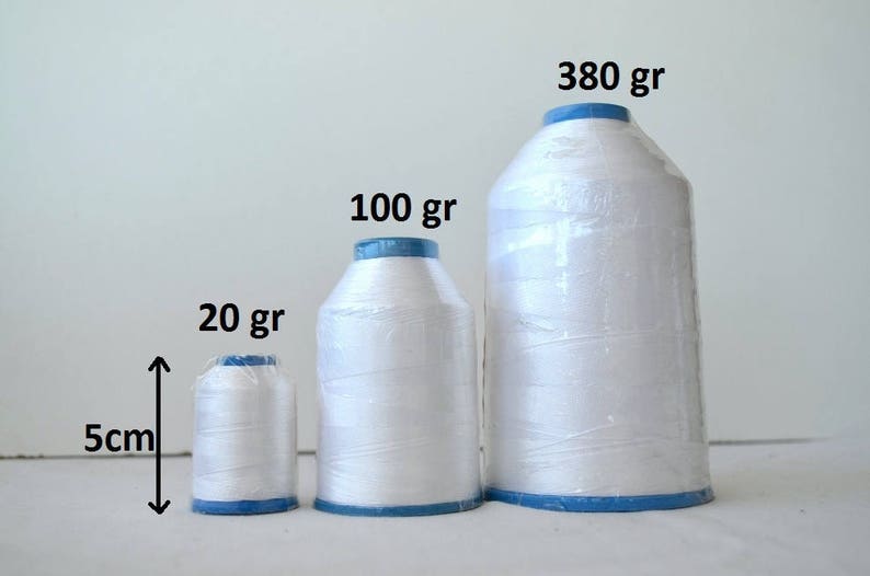 May include: Three spools of white thread, labeled 20 gr, 100 gr, and 380 gr. The spools are arranged in order of size, with the smallest spool on the left and the largest spool on the right. The spools are all wrapped in clear plastic and have blue caps.