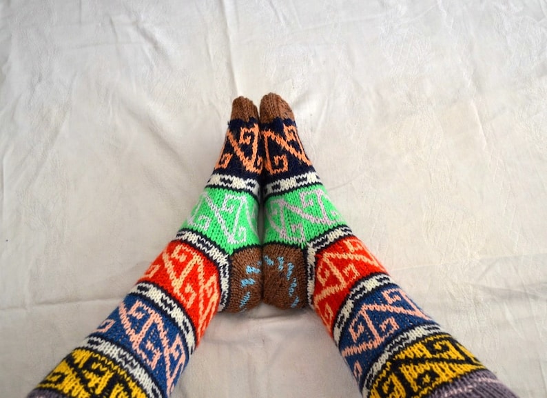 May include: A pair of colorful knitted socks with geometric patterns in shades of blue, green, orange, red, brown, and white.