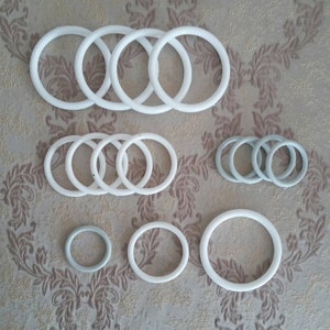 May include: A set of white and gray rubber o-rings of various sizes. The o-rings are arranged in groups on a patterned surface.