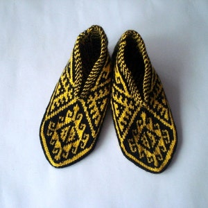 May include: A pair of handmade knitted slippers. The slippers are black with a yellow geometric pattern. The interior and trim are yellow. The slippers are designed to keep feet warm and comfortable.