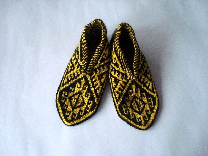 May include: A pair of handmade knitted slippers. The slippers are black with a yellow geometric pattern. The interior and trim are yellow. The slippers are designed to keep feet warm and comfortable.