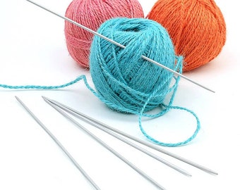 May include: Three balls of yarn, one pink, one orange, and one turquoise blue, with four knitting needles.