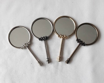 Könnte beinhalten: Vier Handspiegel mit verzierten Blumendesigns und unterschiedlichfarbigen Griffen. Die Spiegel sind rund und haben eine silberne Oberfläche. Die Griffe sind silber, gold und bronzefarben.
